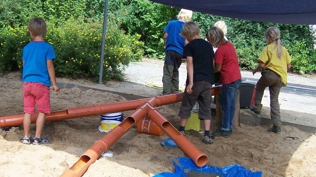 Kinder im Sandkasten beim Wasserohrbau.