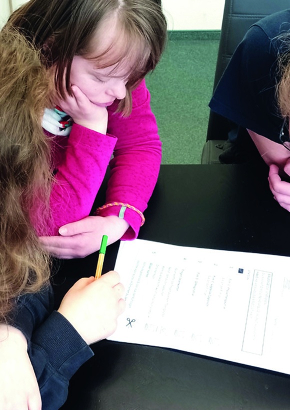 Kind mit Downsyndrom füllt mit Unterstützung Formular aus